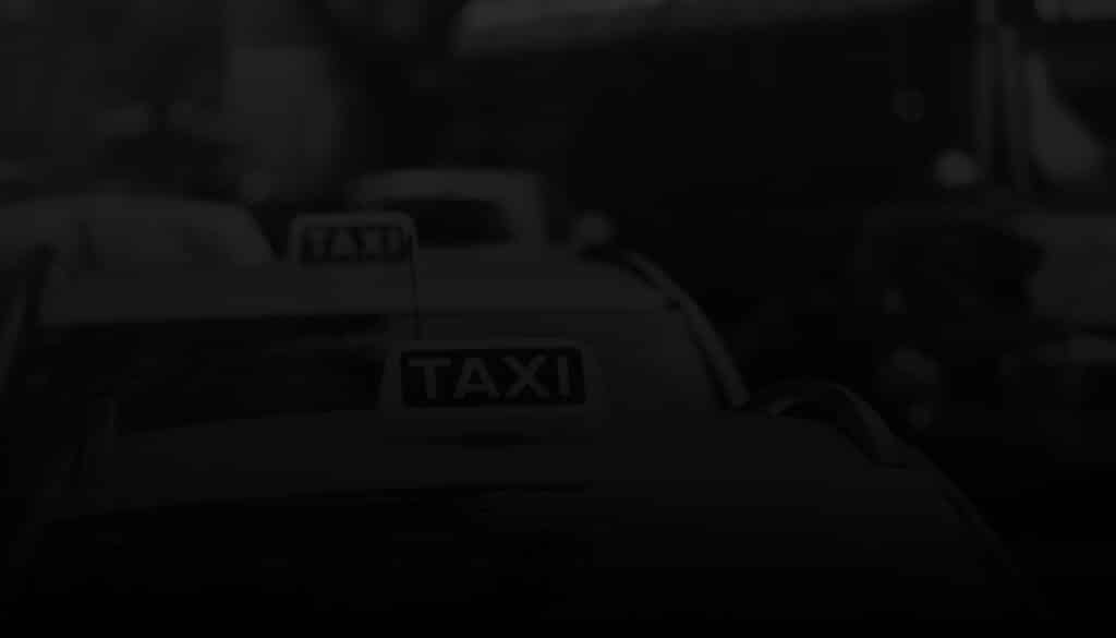 Vue rapprochée des enseignes lumineuses 'TAXI' sur les toits de plusieurs voitures en file.